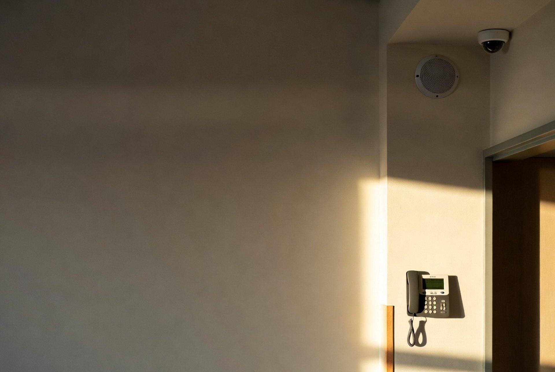 A modern facility corridor where an IP phone, a paging speaker, and a camera dome work as one system