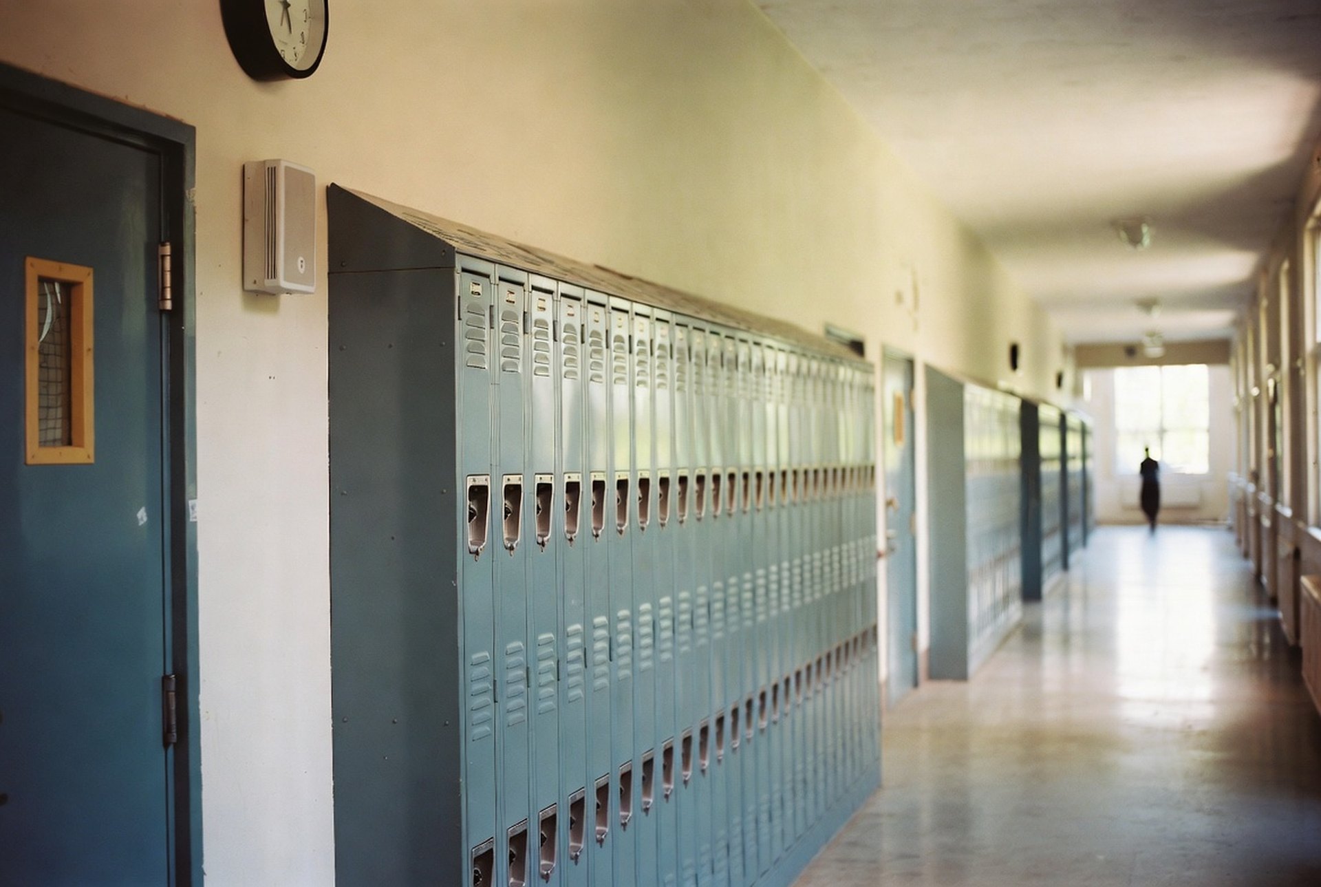 An empty K-12 school hallway with lockers, a wall-mounted paging speaker, and a clock