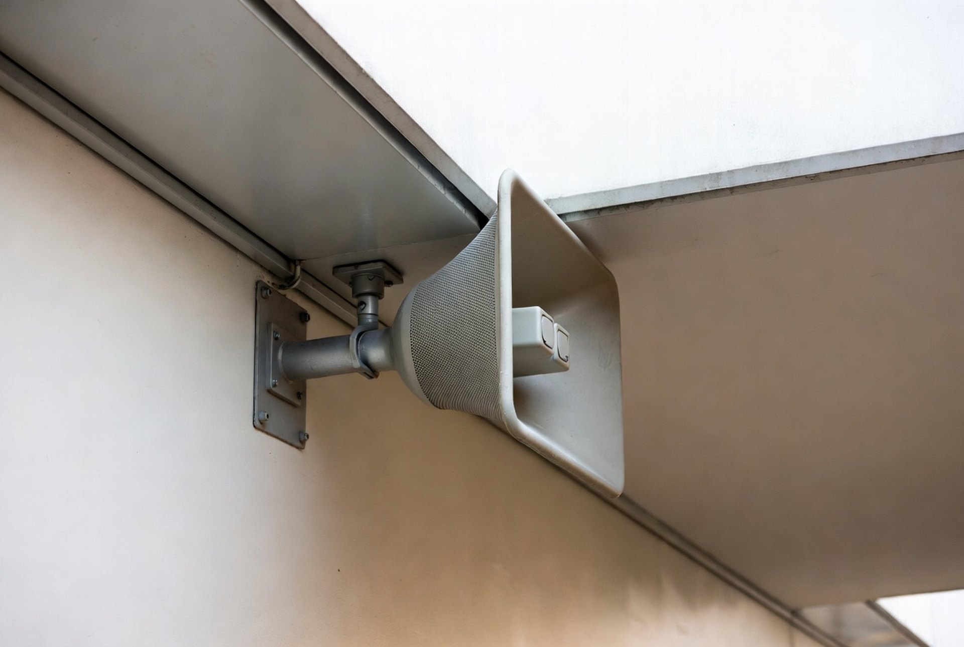 An overhead paging horn speaker mounted near a building eave